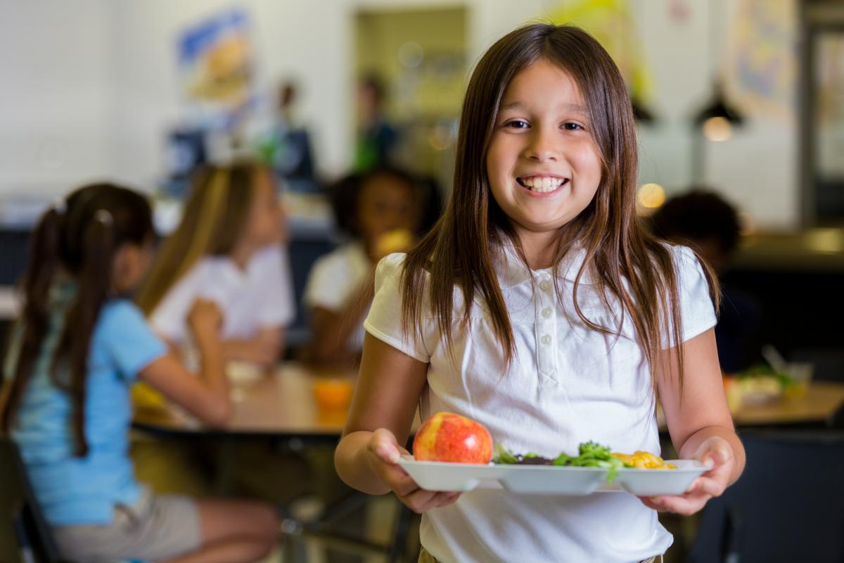 Girl stands with her lunch tray in a cafeteria.