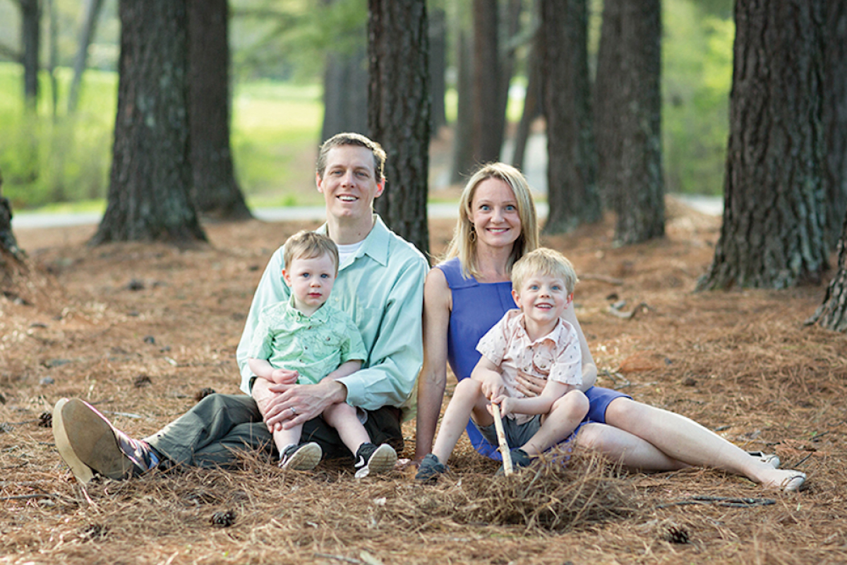 Dr. Kelleher sits on the ground in a forest next to her husband and her two sons.