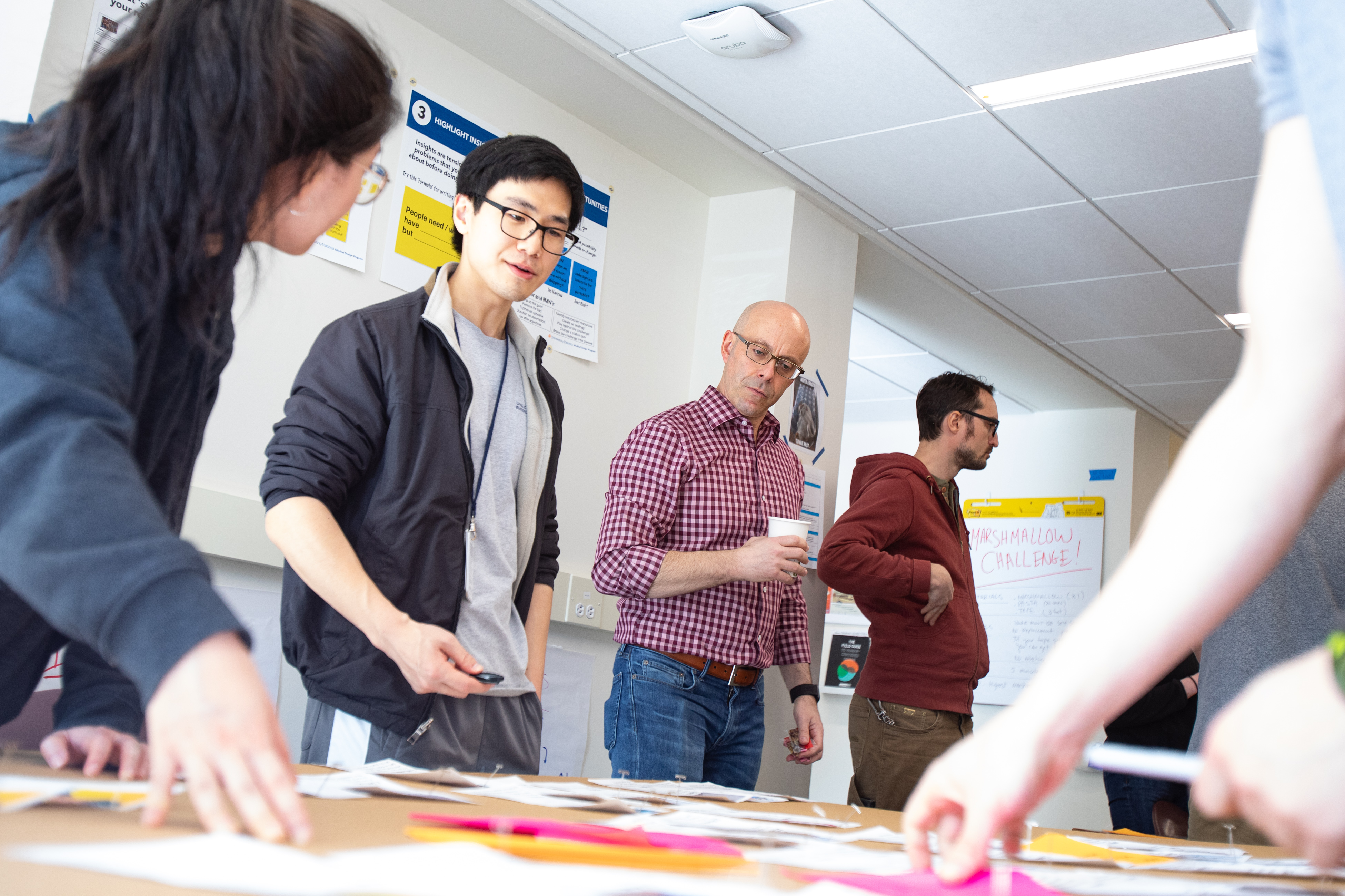 Dr. Matthew Trowbridge stands at a table surrounded by student and leads a Design Thinking workshop with his students.