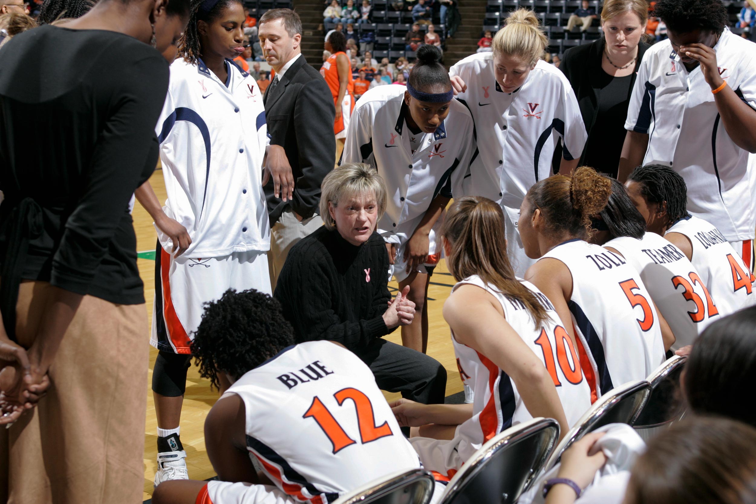 Debbie Ryan sits on the sidelines surrounded by members of the UVA women's basketball team.
