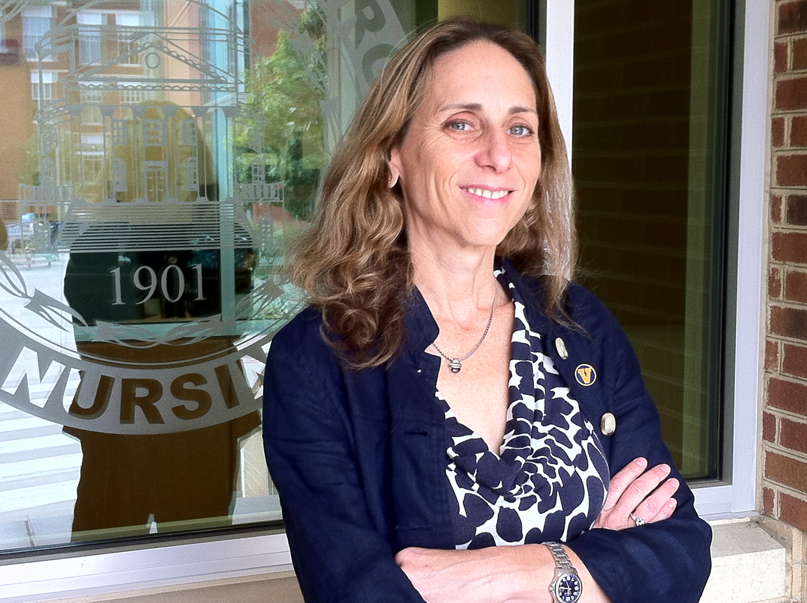 Carol Manning leans against a window with a UVA School of Nursing emblem on it