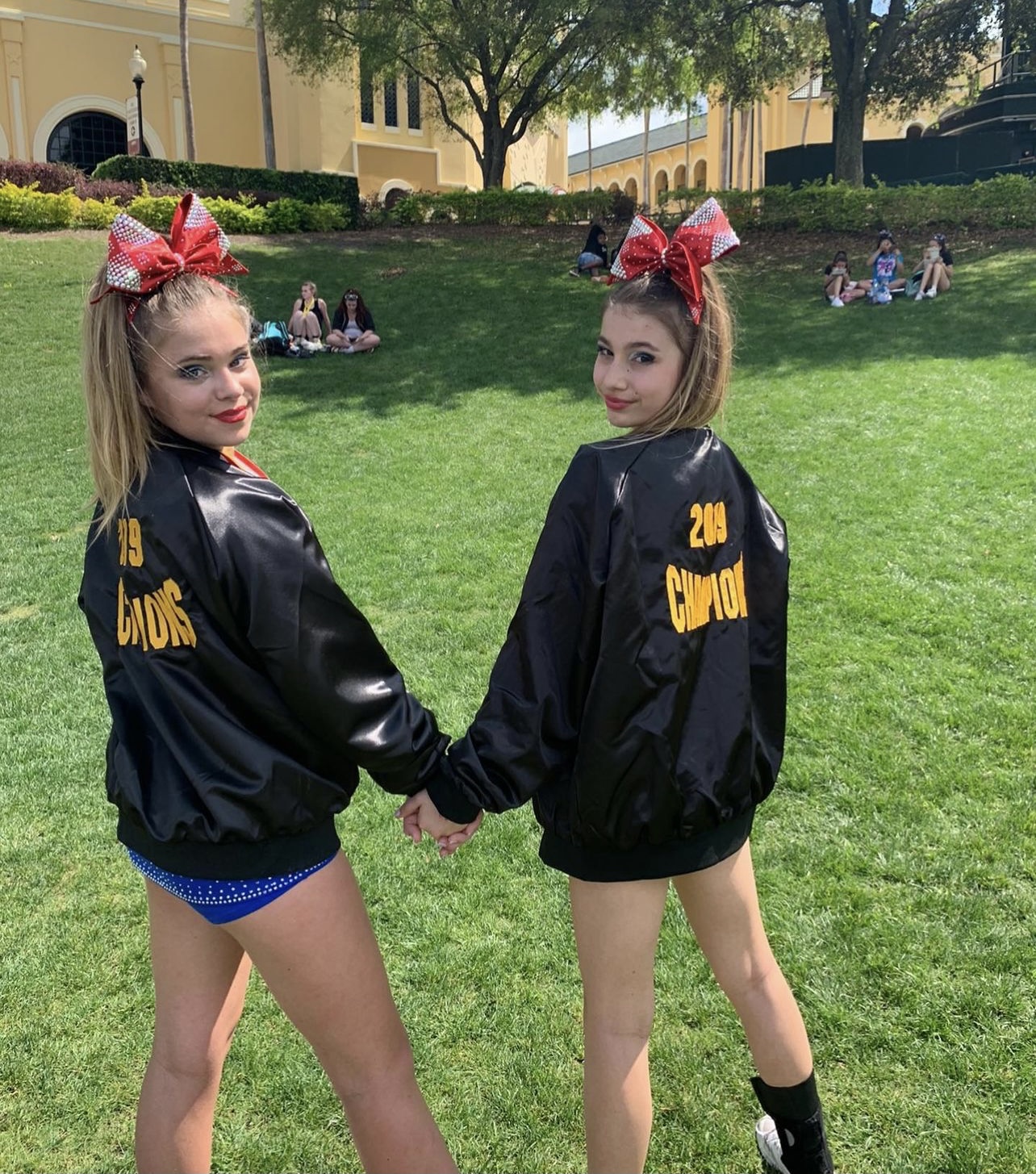 the two girls hold hands in their cheerleading outfits