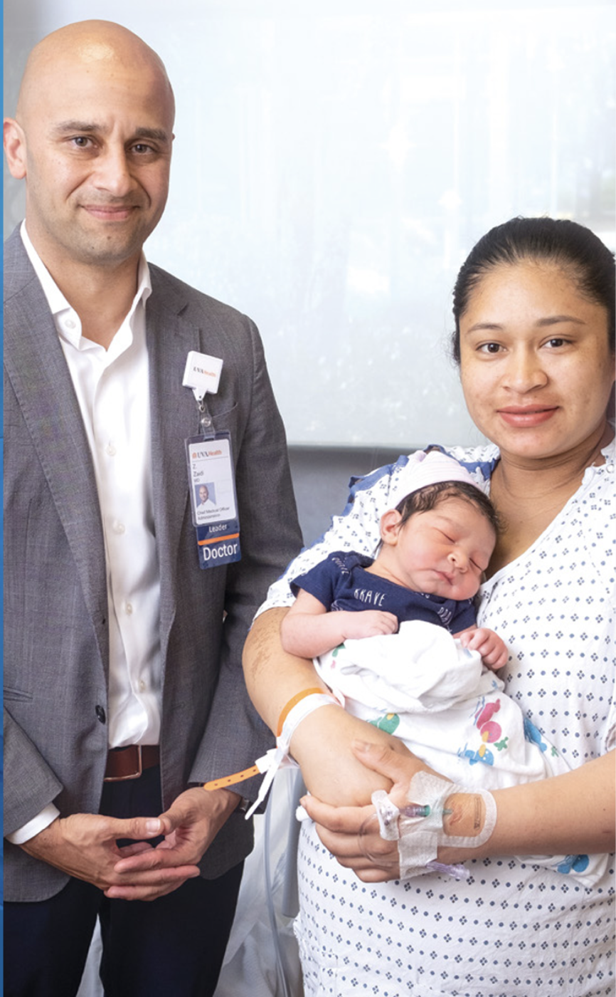 Dr. Zaidi stands next to Keylin Soto as she holds an infant