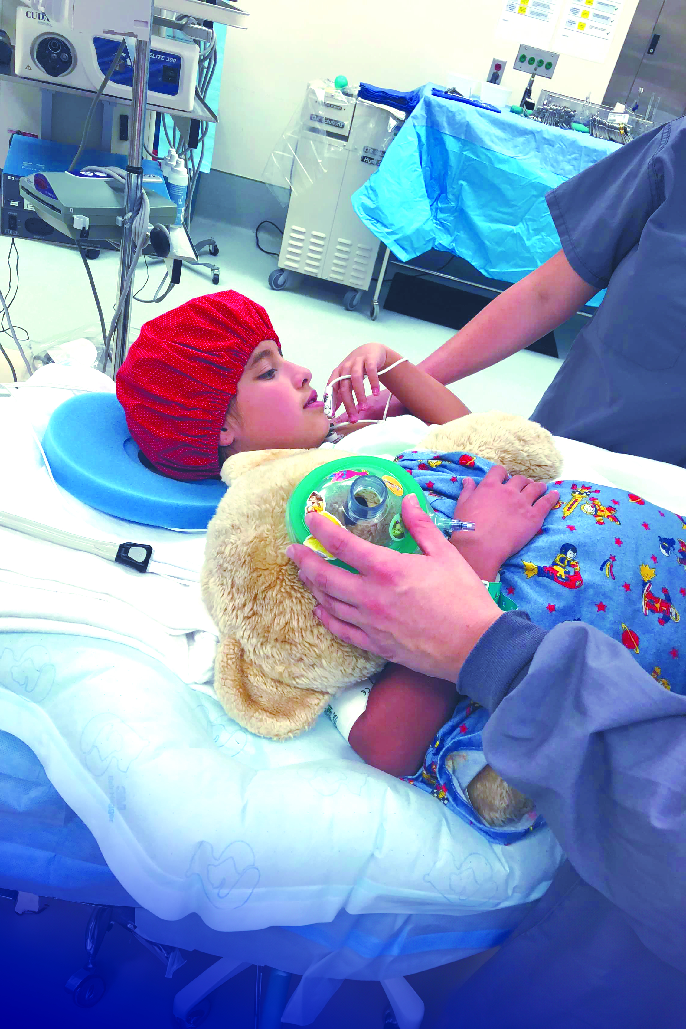 Olivia lays in an operating room holding a stuffed bear 