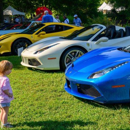 A little girl stands and looks at the sports cars on display