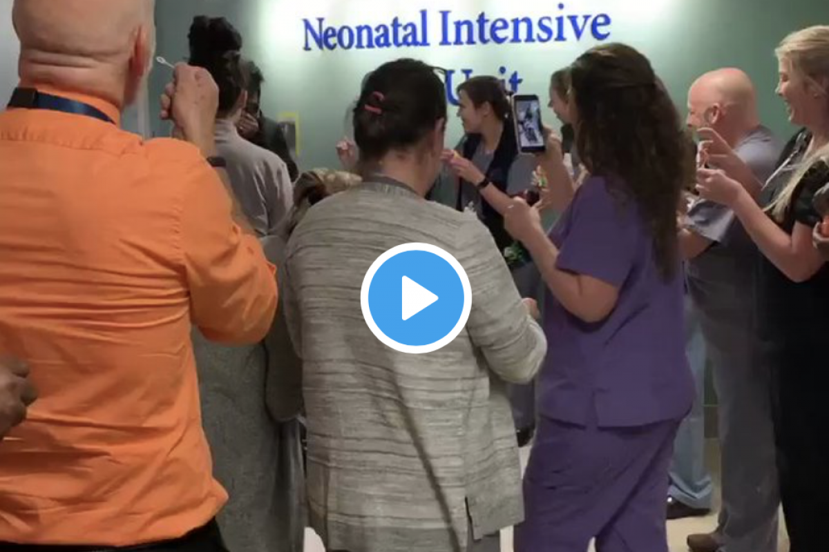 A crowd of caregivers stands outside the NICU clapping.