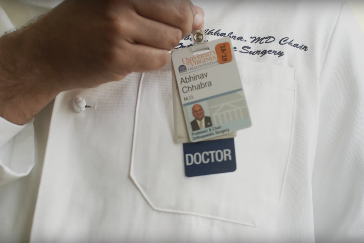 Dr. Chhabra's white coat, you see his hand hooking his medical badge to his pocket.
