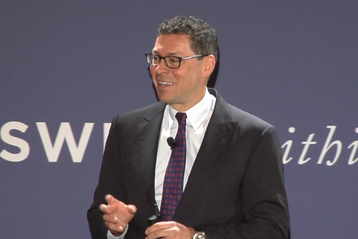 Dr. Oberholzer stands in front of a blue backdrop presenting. 