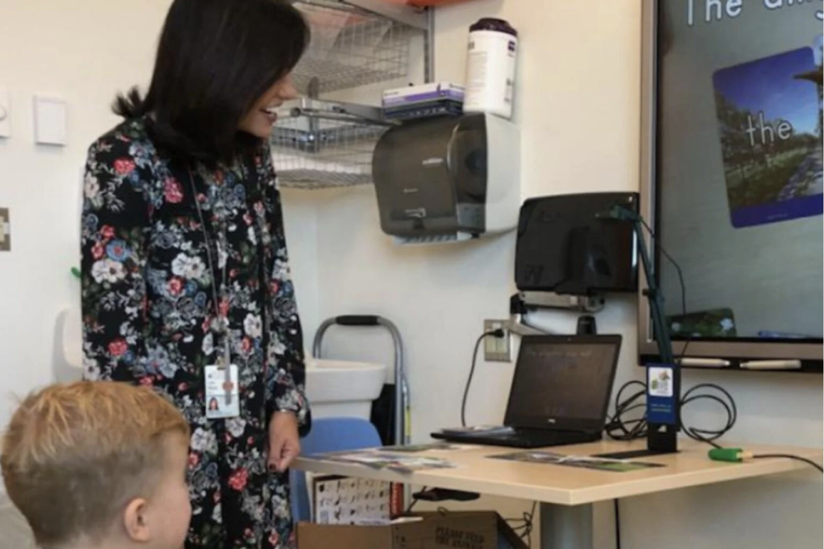woman stands next to boy while he looks at screen