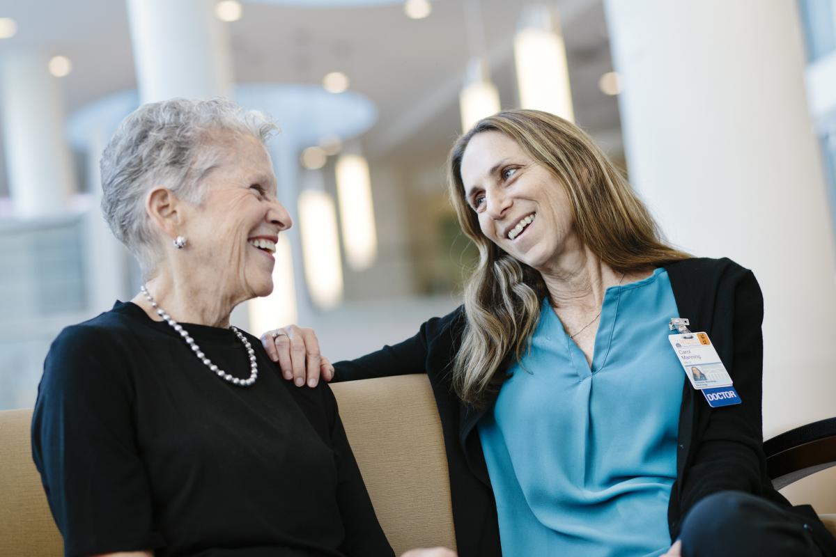 Patient Mary Ann Leeper and Dr. Carol Manning sit together in the hospital lobby and smile.