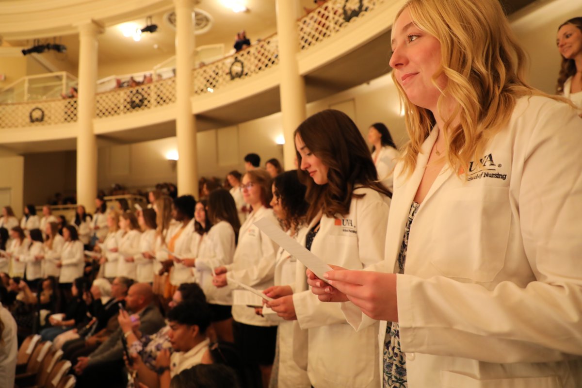 students in white coats stand during a ceremony