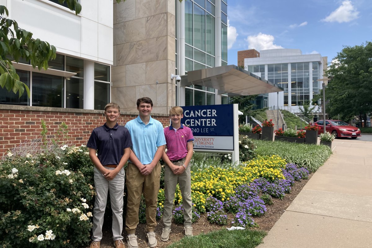 The three boys stand in front of the Emily Couric Cancer Center building.