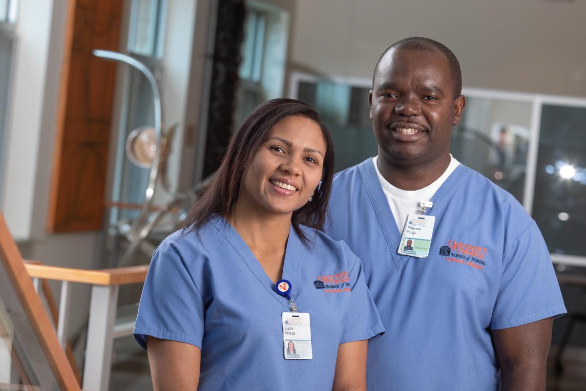 Paterson Ilunga and Lucie Ndaya stand in a classroom and smile in blue scrubs