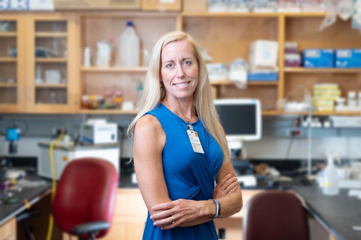 Shayn Peirce-Cottler stands in her lab wearing a blue dress and smiling