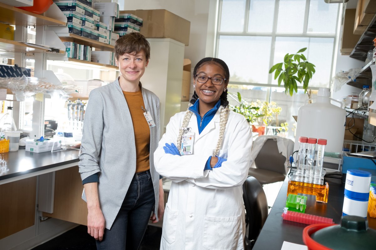 Sarah and Nadia stand in white coats in a lab