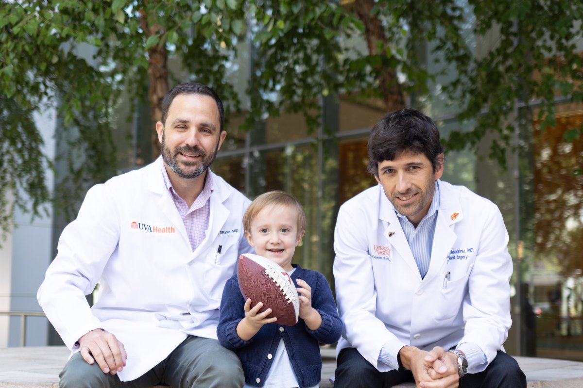 William holds a football and stands between two doctors as they sit outside