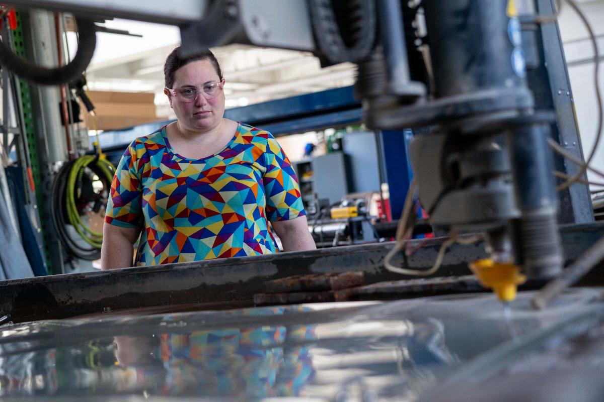 Melissa Goldman watches as a water jet cuts plastic face shields.